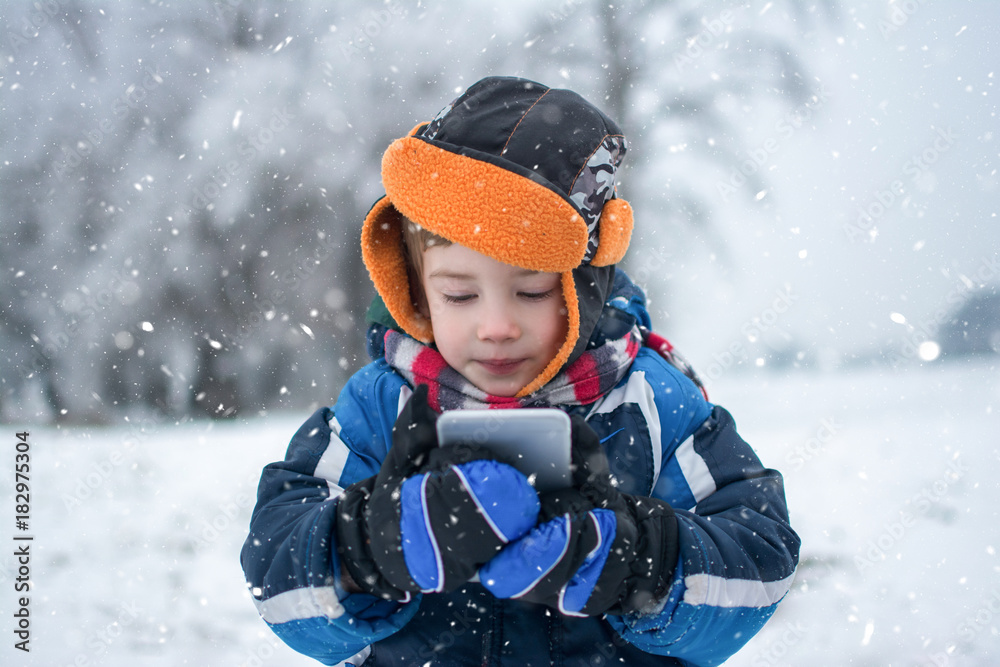 Portrait of little boy with mobile phone on snowy day in winter park. Portrait of little boy with mobile phone on snowy day in winter park.