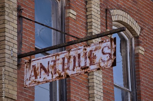 Antique metal rusty sign outside of old brick buildings in business district