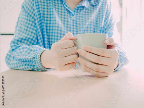 close up white hot coffee cup for drink in morning time in hand of beauty asian girl in blue pajamas at her bedroom