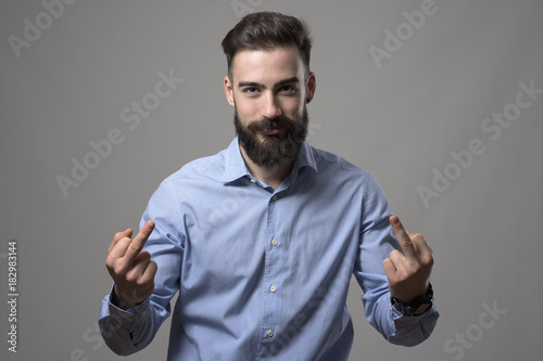 Bossy young bearded business person showing middle finger obscene rude gesture with both hands looking at camera over gray background. 