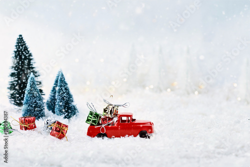 1950's antique vintage red truck hauling a Christmas gifts home through a snowy winter wonder land with pine trees. Extreme shallow depth of field with selective focus on vehicle.