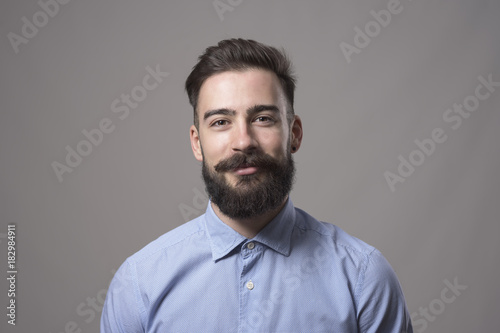 Horizontal  head and shoulder portrait of young bearded business man smiling at camera against gray studio background. photo