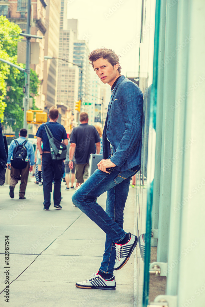 European College Student in New York. Wearing blue blazer, jeans, sneakers,  holding laptop computer, a young guy standing against glass wall on street.  People walking on background. . Stock Photo | Adobe Stock
