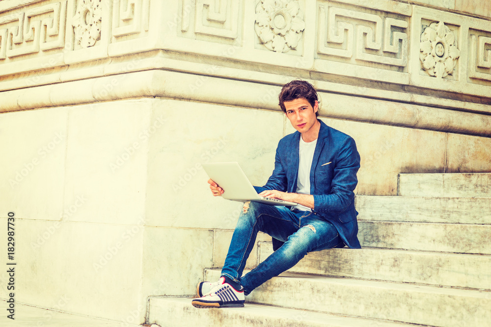European college student studying in New York. Wearing blue blazer, jeans,  sneakers, a young guy sitting on stairs on campus, reading, thinking,  working on laptop computer. . Stock-Foto | Adobe Stock