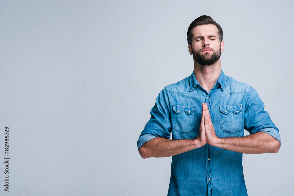 Calming down. Handsome young man paying and keeping eyes closed while standing against white background Calming down. Handsome young man paying and keeping eyes closed while standing against white background