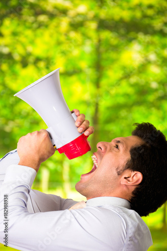 Portrait of a handsome man shouting with a megaphone in a blurred green background