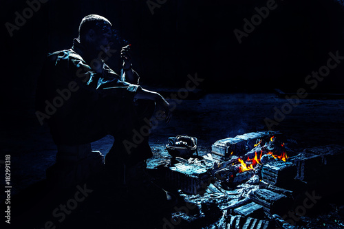 Fototapeta Naklejka Na Ścianę i Meble -  Special forces soldier after the fight sitting by the fire in ruined building smoking cigarette