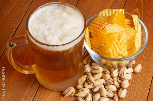 Top view of a full mug of beer with foam, chips, pistachios