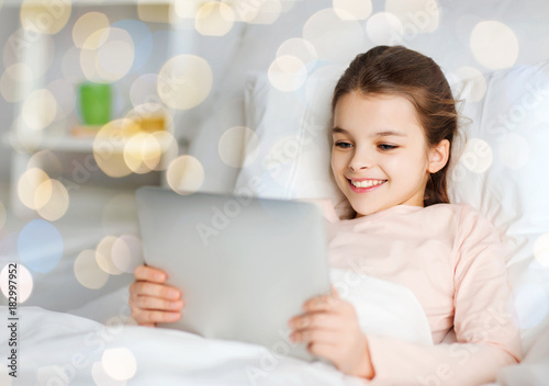 happy girl in bed with tablet pc over lights