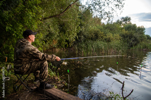 the lake on the edge of the forest, man during sunset closeup of fishing rod