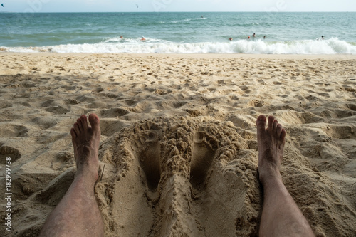 Close up of a man feet relaxing on an tropical beach near the sea. Concept of rest or vacation in summer