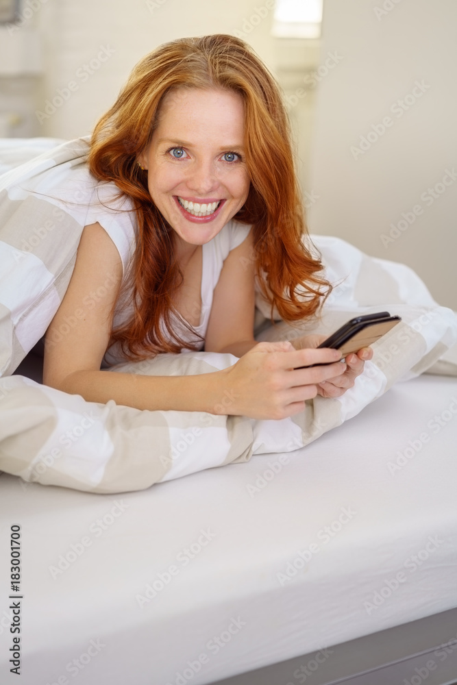 frau liegt im bett und hält ihr smartphone in der hand frau liegt im bett und hält ihr smartphone in der hand
