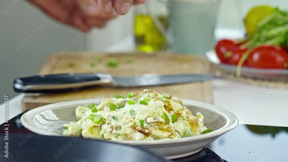 Close up of hands of male cook adding chopped spring onion to tasty scrambled eggs on plate Close up of hands of male cook adding chopped spring onion to tasty scrambled eggs on plate