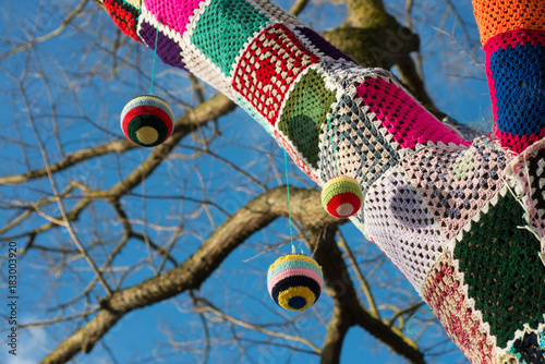 knitted woollen yarn bomb tree with baubles and blue sky background photo