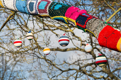 knitted woollen yarn bomb tree with baubles and blue sky background photo