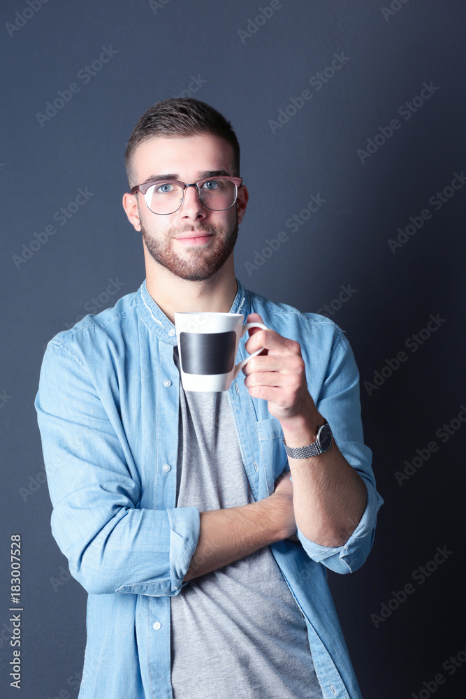 Portrait of a handsome young man standing and holding a cup of coffee in his hands Portrait of a handsome young man standing and holding a cup of coffee in his hands