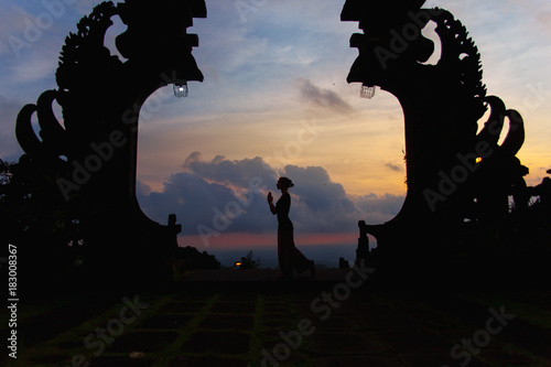 Silhouette of woman full length at the balinese traditional gates at the top of Pura Besakih at sunset.
