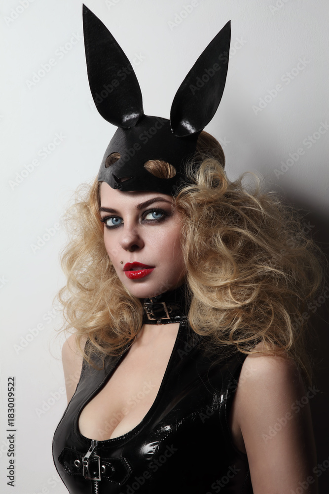 Vintage style young slim sexy woman in black vynil dress and fetish leather rabbit mask