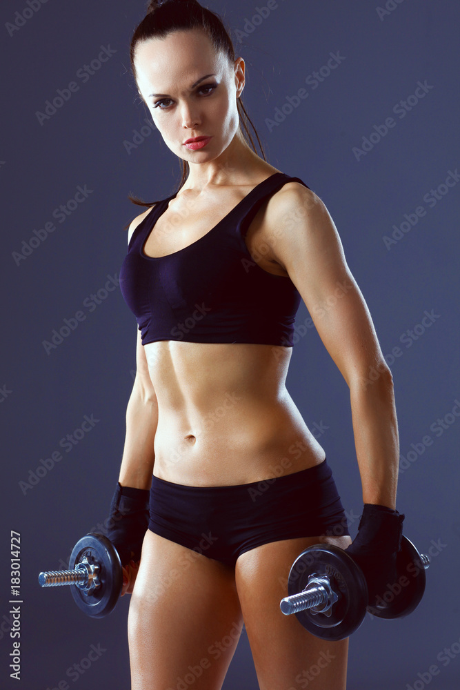 Muscular young woman standing on gray background. Muscular young woman Muscular young woman standing on gray background. Muscular young woman