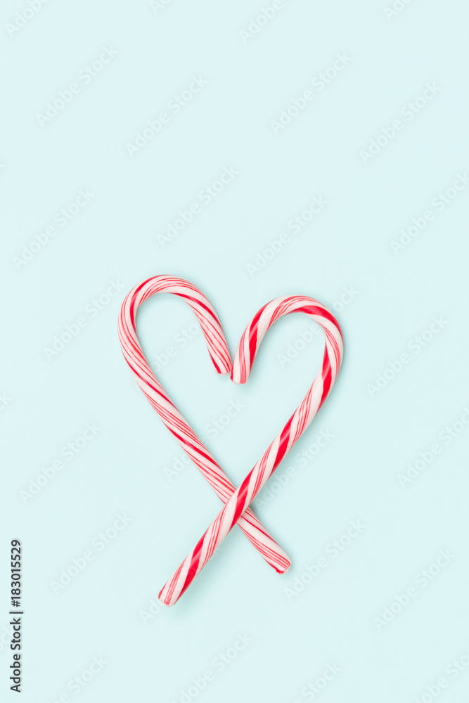 Top view on mint hard candy cane striped in Christmas colours in shape of a heart isolated on a turquoise background. Closeup. Christmas, holidays season.