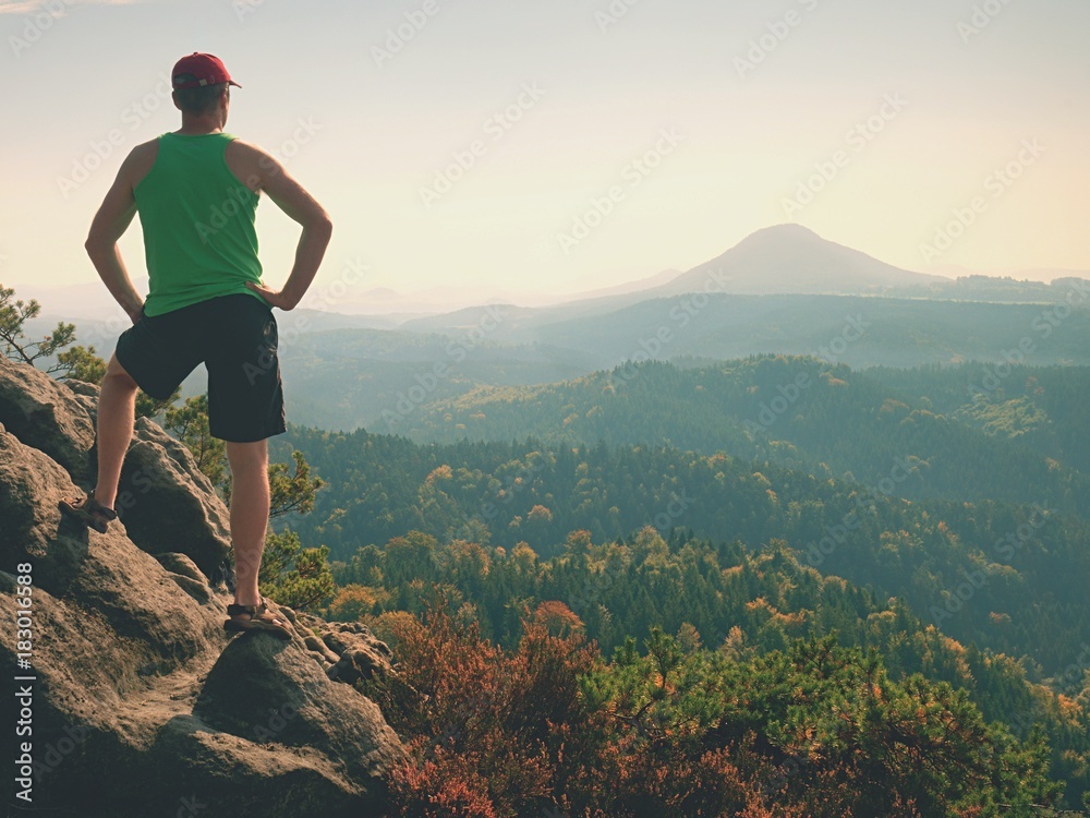 Tourist in green singlet and black shorts on rock, enjoy nature scenery. Valley in sun bath