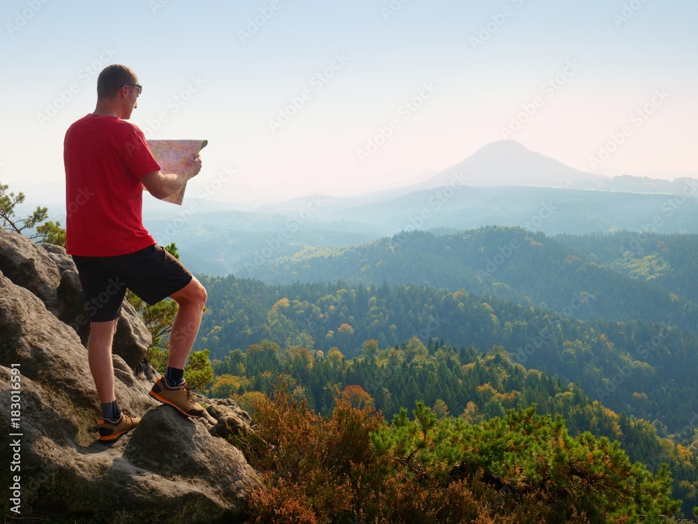 Lost tourist  on peak looking into landscape  while check paper map, hiking  in nature.