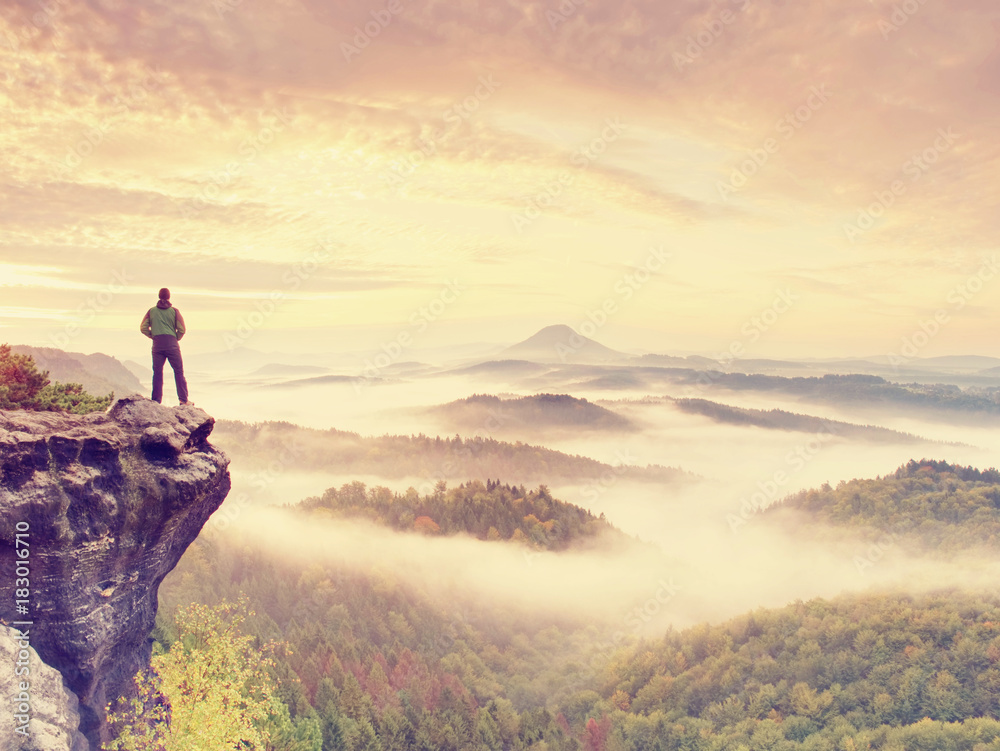 Fototapeta premium Man stay on rocky peak within daybreak and watch over misty landscape.