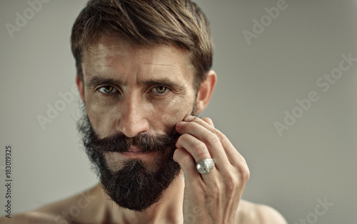 Portrait of middle-aged handsome man with bare shoulders. Lush and dense beard and moustache in a hipster style on the wrinkled face of the adult man. Sincere and thoughtful look at the camera.
