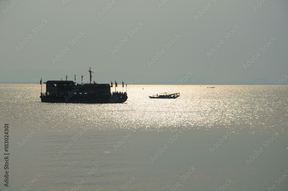 A silhouette of a tourist boat and fishing boat on the waters of Tai Lake, Taihu outside of the three kingdoms city scenic area in Wuxi China in Jiangsu province as the sun sets.