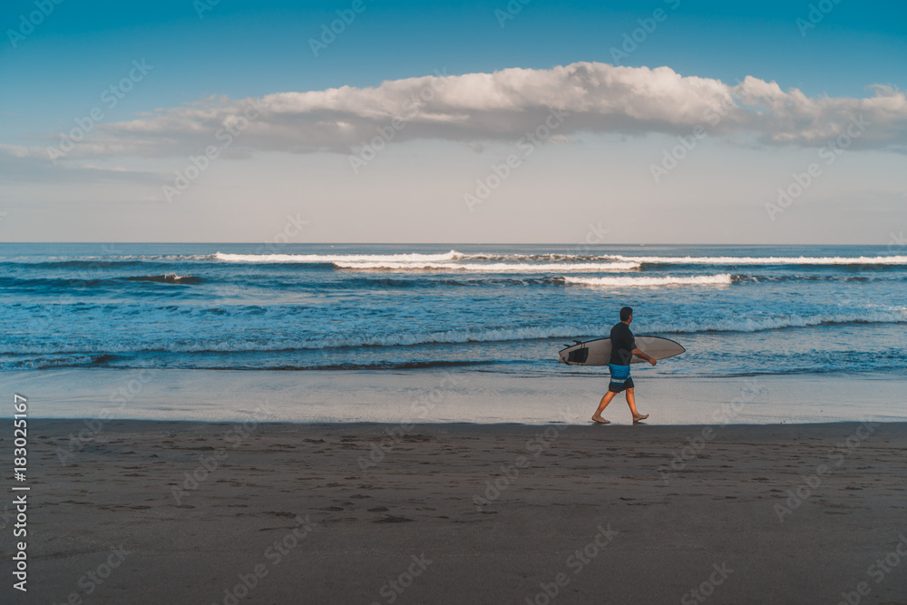 Surfer with his surfboard walking along the cuta beach, Bali