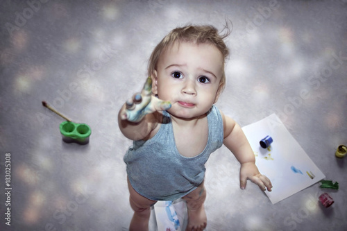 Cute little boy with his hands dirty in paints showing his finger on the camera
