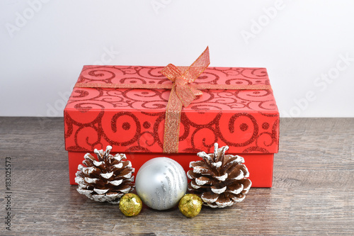Christmas scene including wrapped package, frosted pine cones, and ornaments on rustic wood table and white background