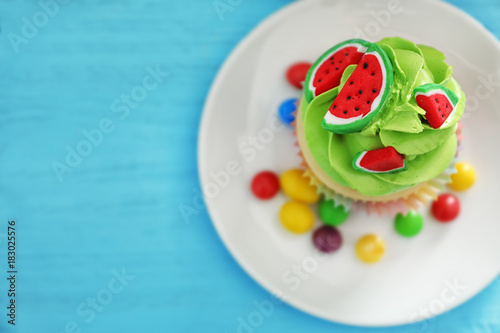 Plate with tasty colorful cupcake on wooden background