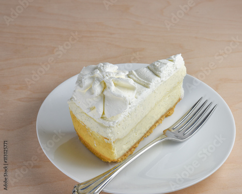 Isolated vanilla cheescake with a layer of whipped cream and fork on a hickory wood table