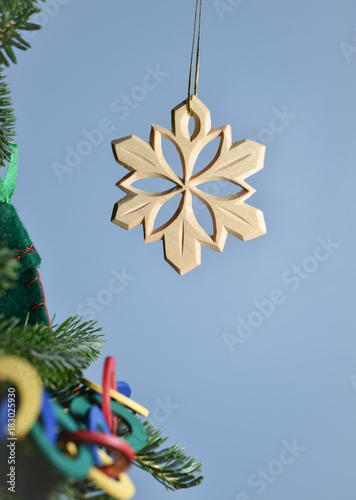 Hand carved wooden snow flake ornament hanging at edge of a decorated Christmas tree.