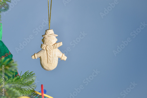 Isolated hand carved wooden snowman ornament at edge of Christmas tree with copy space. Light blue background.