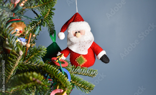 Stuffed Santa Claus  ornament hanging at edge of a decorated Christmas tree with room for text or copyspace.