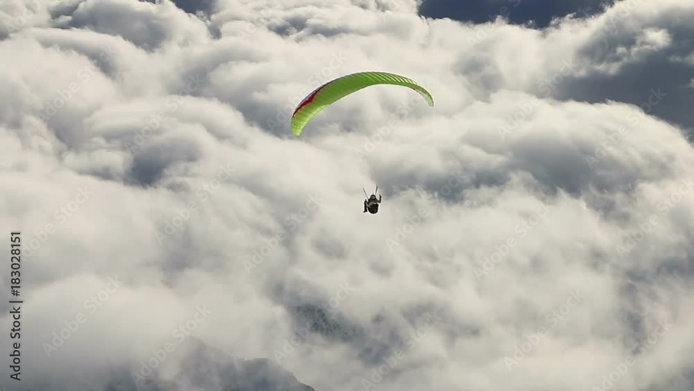 Paragliding above mountain peaks and clouds during winter sunny snowy day