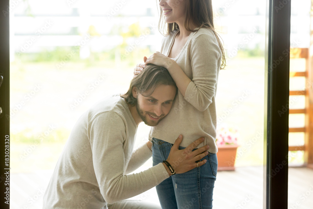 Φωτογραφία Happy young man putting ear to pregnant womans belly listening to baby moving in
