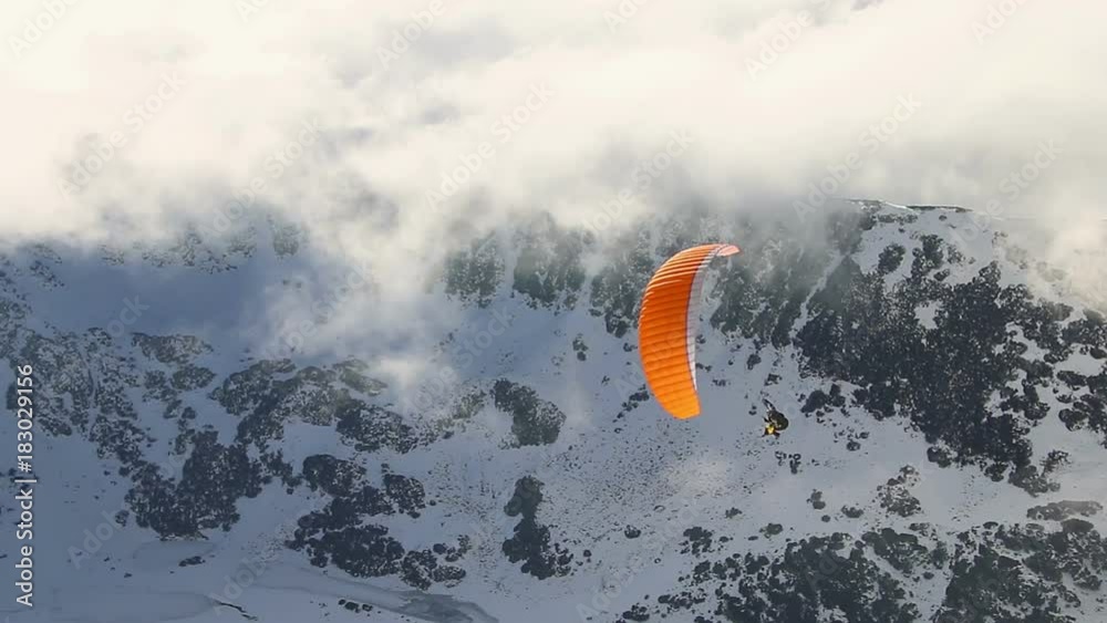Paragliding above mountain peaks and clouds during winter sunny snowy day