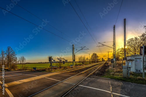 Obraz na plátně Beautiful blue and yellow sunset on level crossing, double track with passing tr