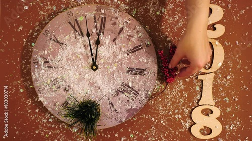 Female hands decorating the New Year's clock with a bump, tisels, maple leafs, rowan and a Santa toy. The number 2018 and snow on a brown background. Top view photo