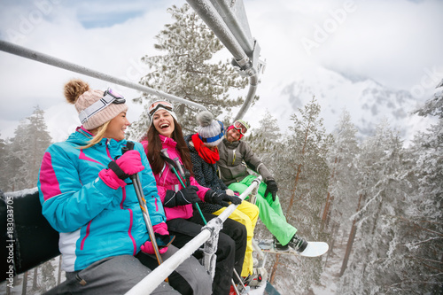 happy friends enjoying in winter vacations. They ride up ski lift at snowy day