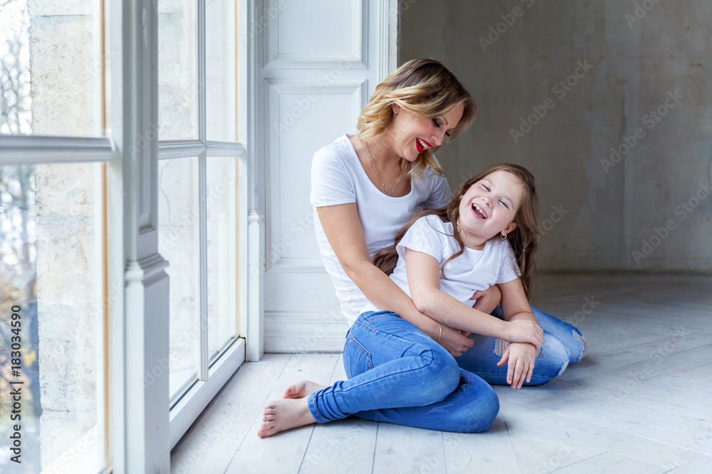 Young mother holding her child. Woman and little girl relax in a white bedroom near the window. Happy family at home. Young mother playing with her daughter Young mother holding her child. Woman and little girl relax in a white bedroom near the window. Happy family at home. Young mother playing with her daughter