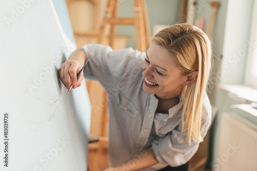 Beautiful blonde woman artist drawing with a brush and pain in her art studio