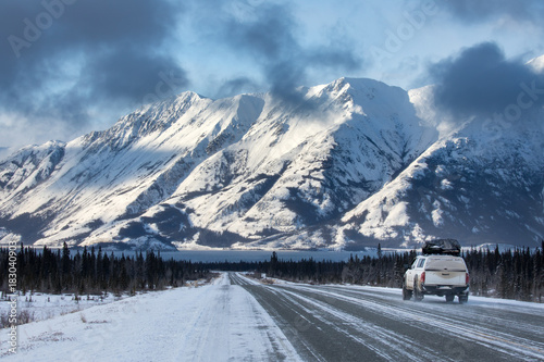 A car driving towards mountains on the Alaska Highway photo