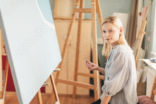 Beautiful blonde woman artist drawing with a brush and pain in her art studio