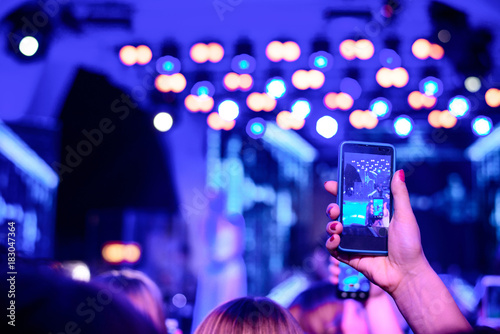 Fan taking photo of concert at festival, night club party, rock concert. Hand with a smartphone records performance. People at concert shooting video or photo.