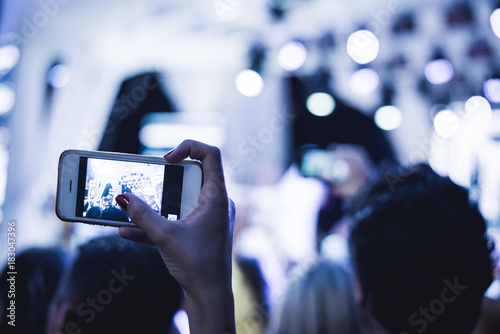 Fan taking photo of concert at festival  night club party  rock concert. Hand with a smartphone records performance. People at concert shooting video or photo.