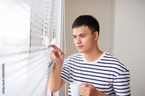 young man having a cup of coffee while looking out of the window at home. photo